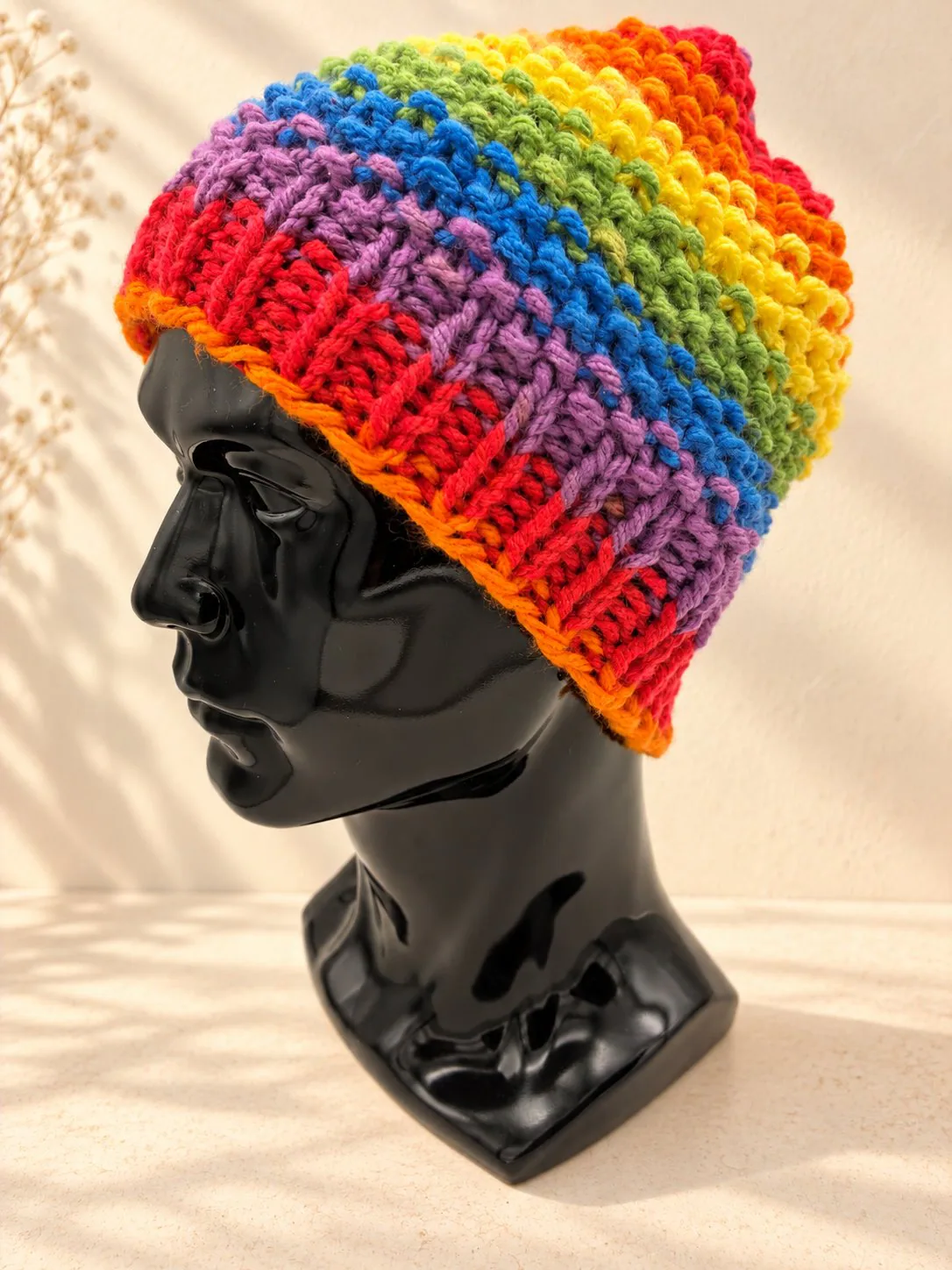 Handgestrickte Kindermütze in Regenbogenfarben im Farbverlauf, Produktfoto.