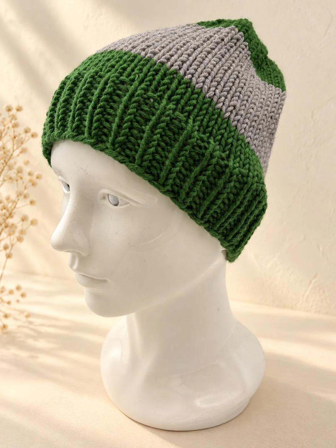 Handgestrickte Mütze in Grün und Grau, Produktfoto.
