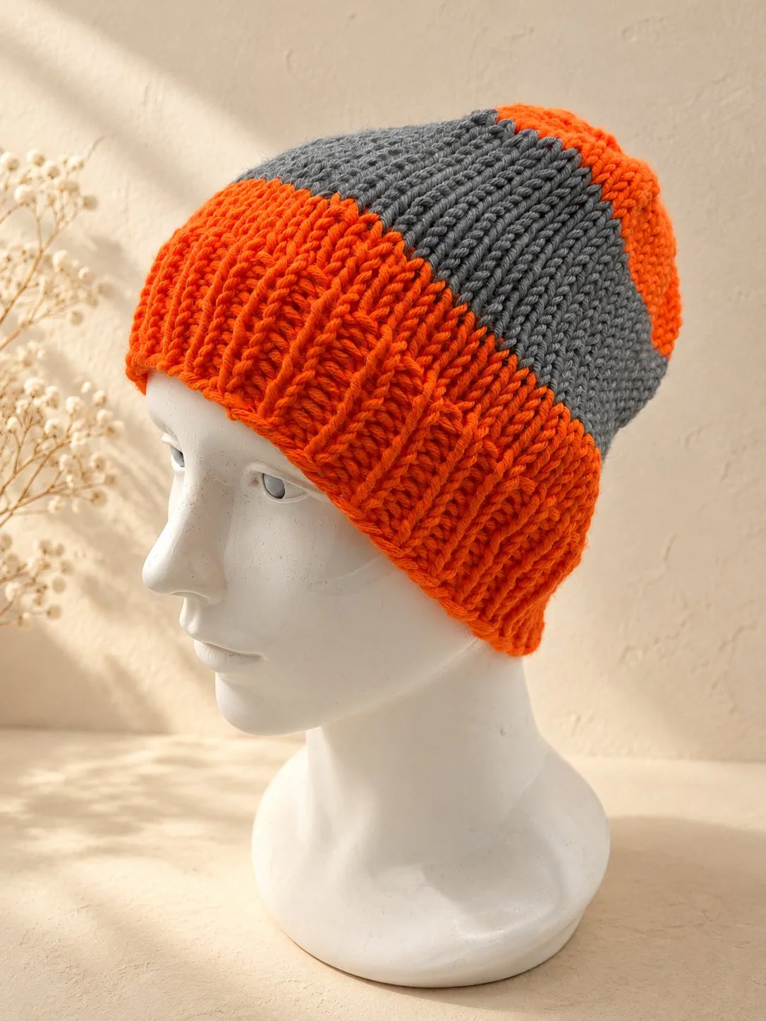 Handgestrickte Mütze in Orange und Grau, Produktfoto.