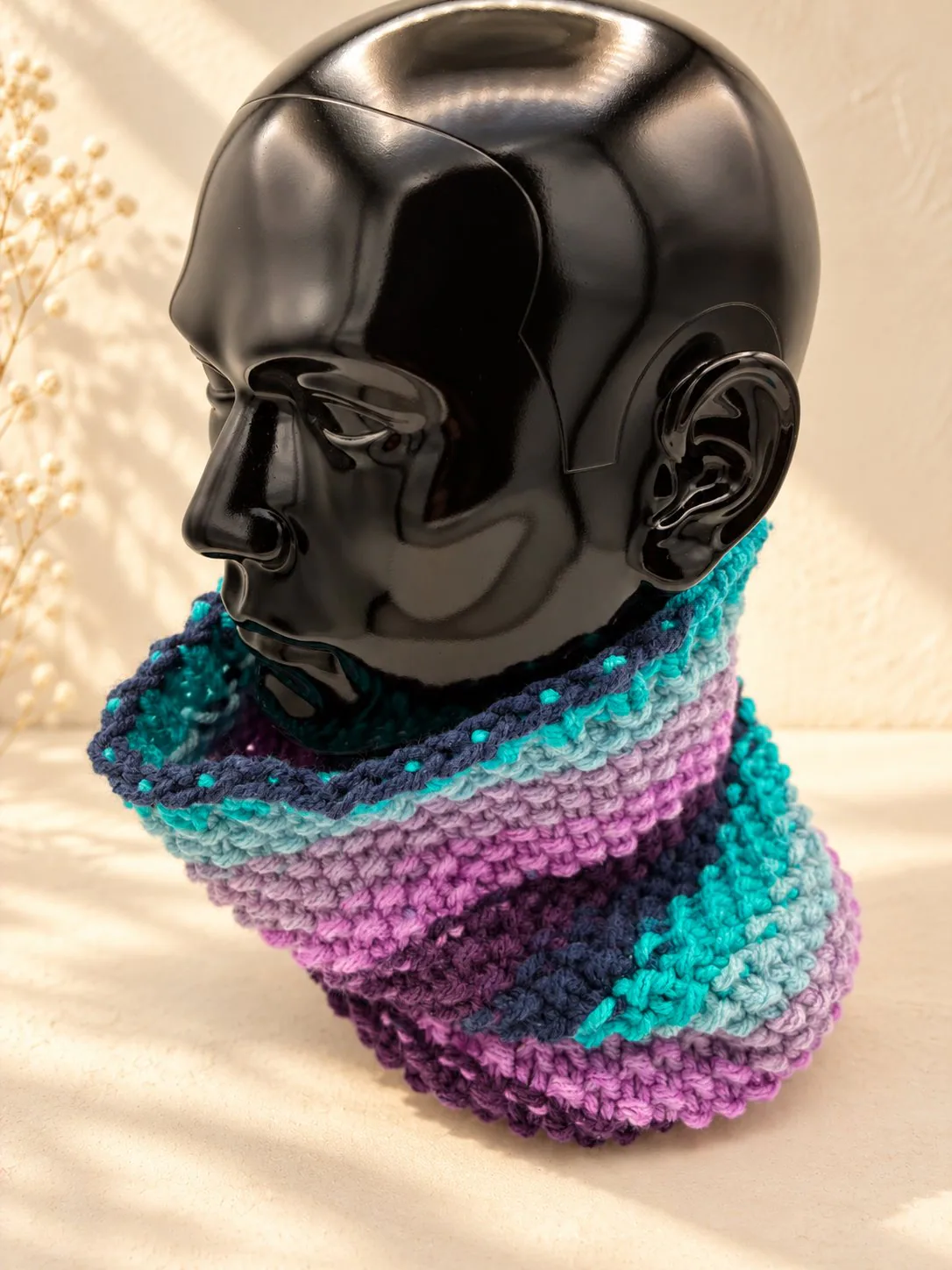 Handgestrickter Schlauchschal in Lila und Rosa, Produktfoto auf schwarzer Büste.