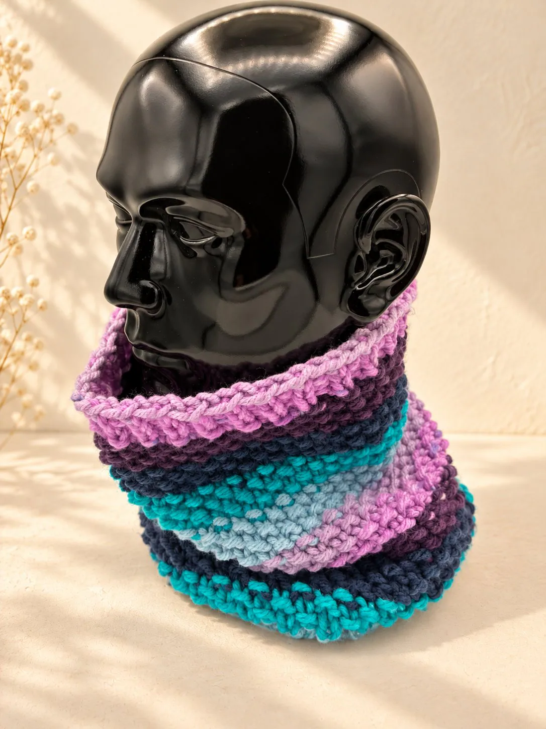 Handgestrickter Schlauchschal in Lila und Türkis, Produktfoto auf schwarzer Büste.