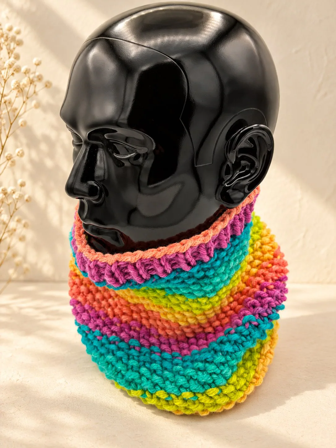 Handgestrickter Schlauchschal in Regenbogenfarben, Produktfoto auf schwarzer Büste.