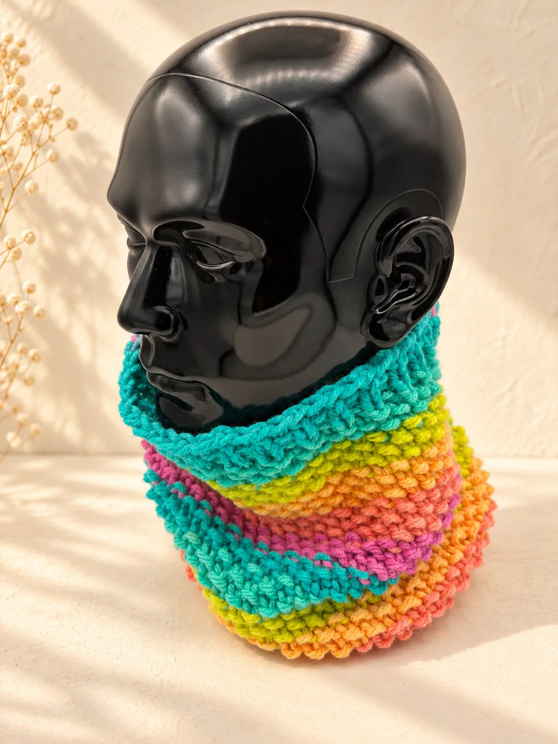 Handgestrickter Schlauchschal in Türkis und Lila, Produktfoto auf schwarzer Büste.